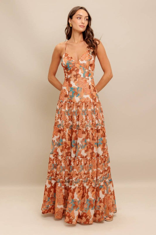 A printed woven maxi dress featuring cami top, straps, drop waist, tiered skirt, O ring back with straps and zipper closure