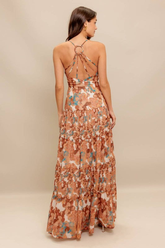 A printed woven maxi dress featuring cami top, straps, drop waist, tiered skirt, O ring back with straps and zipper closure