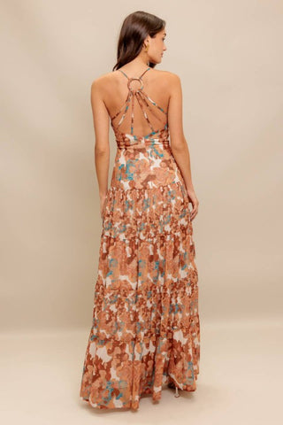 A printed woven maxi dress featuring cami top, straps, drop waist, tiered skirt, O ring back with straps and zipper closure
