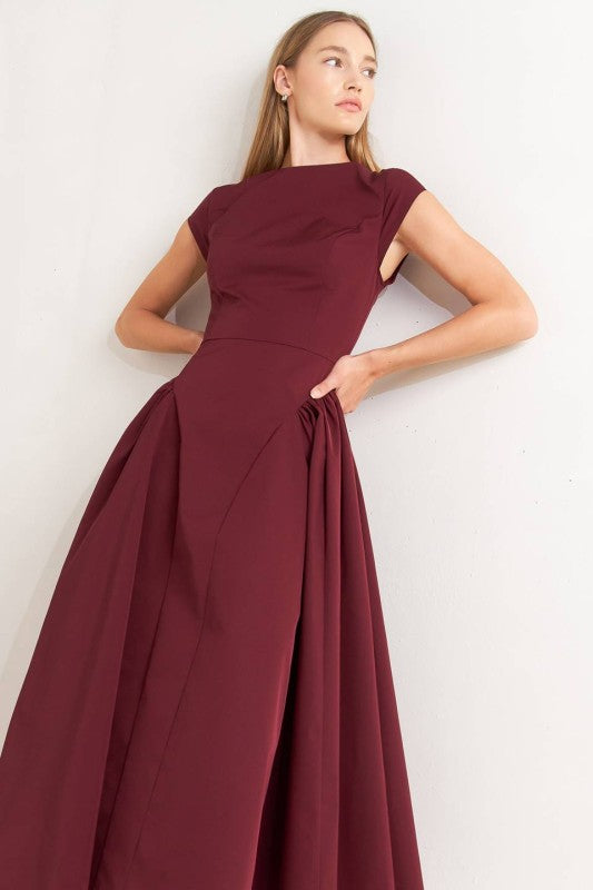 A solid woven midi dress featuring wide neckline, cap sleeve, side shirred full skirt, back cut out and button zipper closure