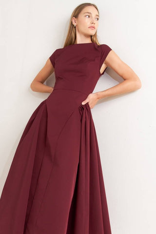 A solid woven midi dress featuring wide neckline, cap sleeve, side shirred full skirt, back cut out and button zipper closure