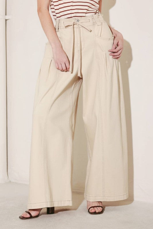 A solid woven pant featuring front closure, elastic waist with tie, pockets and wide leg.