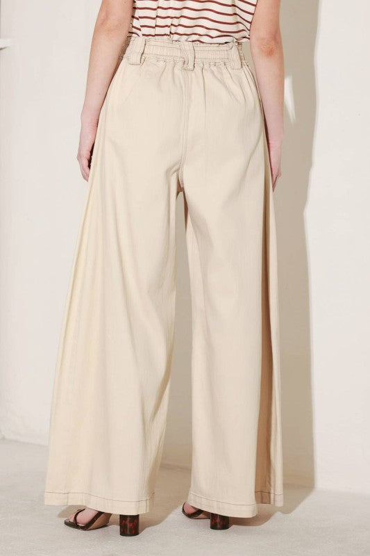 A solid woven pant featuring front closure, elastic waist with tie, pockets and wide leg.