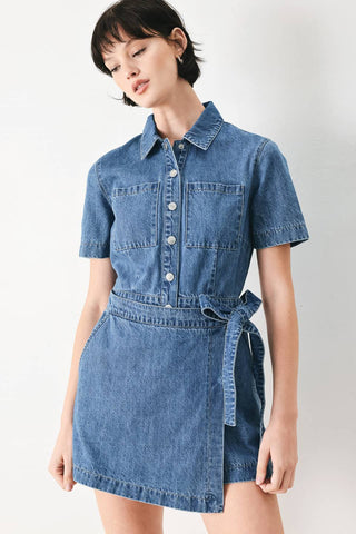 A washed denim skort romper featuring front closure, short sleeve, pockets and side tie