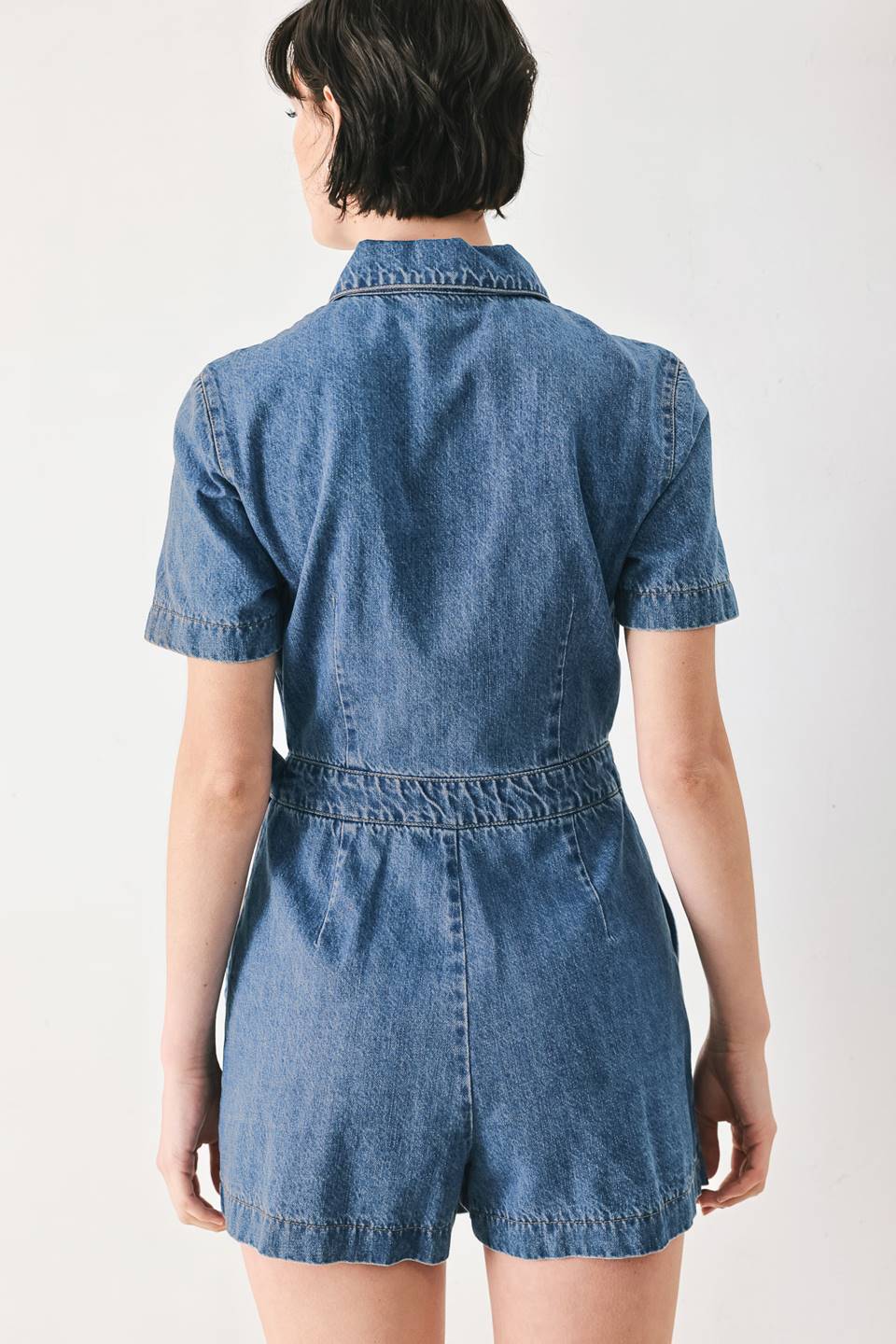 A washed denim skort romper featuring front closure, short sleeve, pockets and side tie