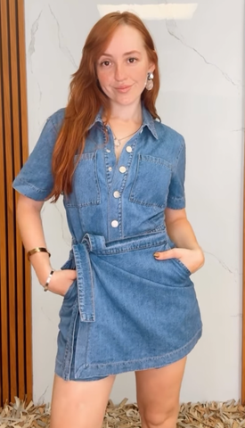 A washed denim skort romper featuring front closure, short sleeve, pockets and side tie