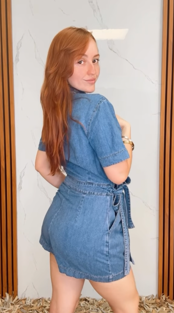 A washed denim skort romper featuring front closure, short sleeve, pockets and side tie