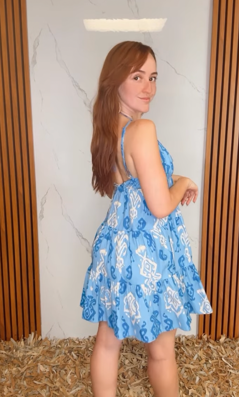 A printed woven mini dress featuring cami top, elastic empire, tier skirt and bare back with back neck tie