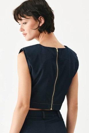 A solid woven crop top with round neckline, sleeveless, hardware detail and back zipper closure.