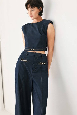 A solid woven crop top with round neckline, sleeveless, hardware detail and back zipper closure.