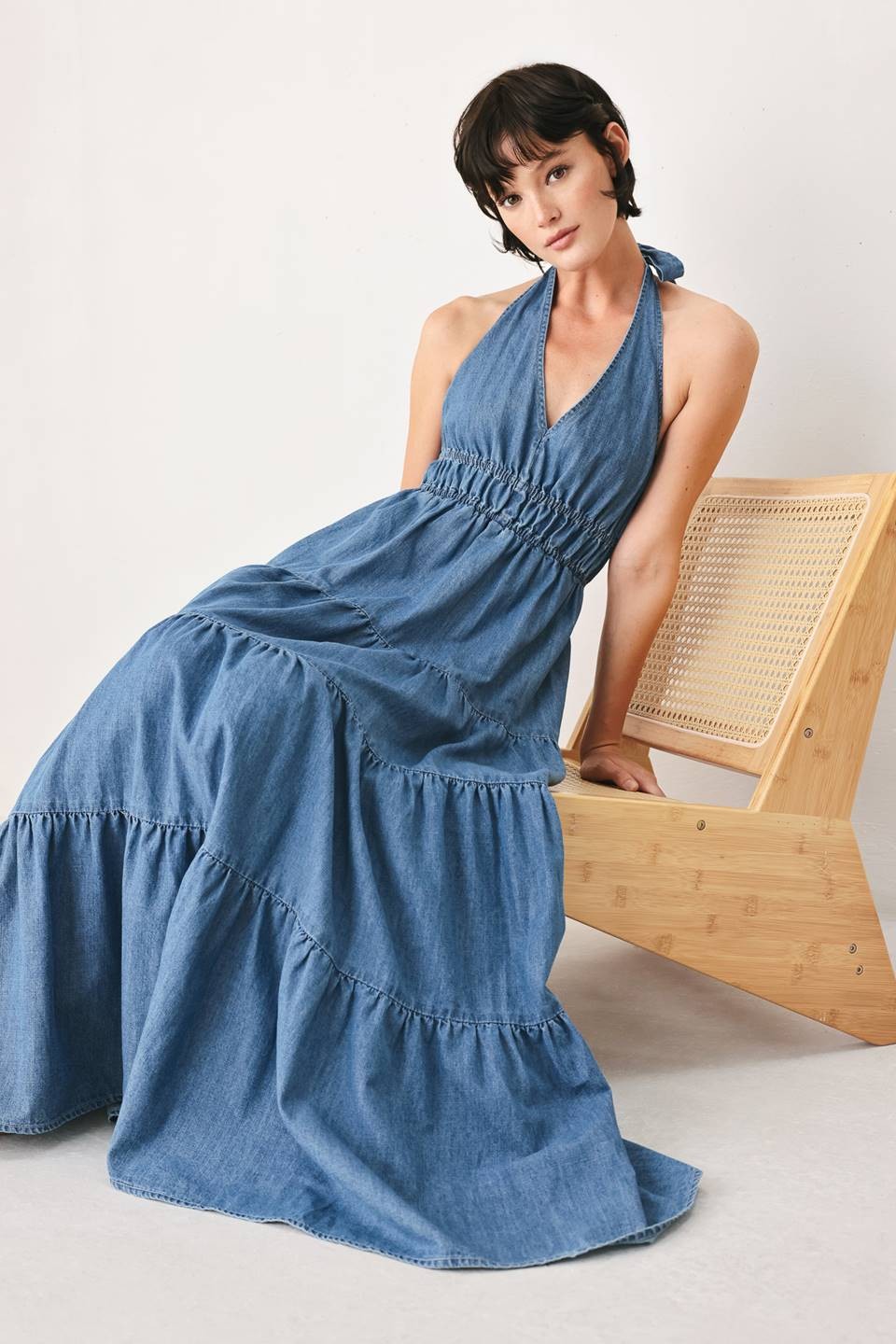 A washed denim midi dress featuring halter neckline, elastic waist, tier skirt, bare back with tie