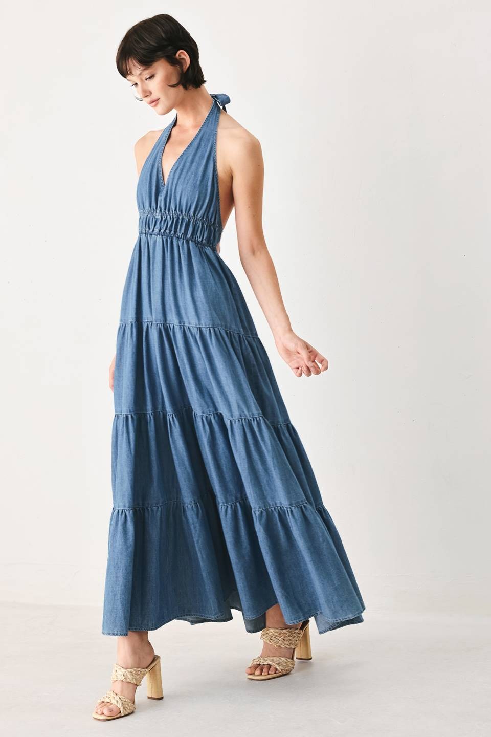 A washed denim midi dress featuring halter neckline, elastic waist, tier skirt, bare back with tie