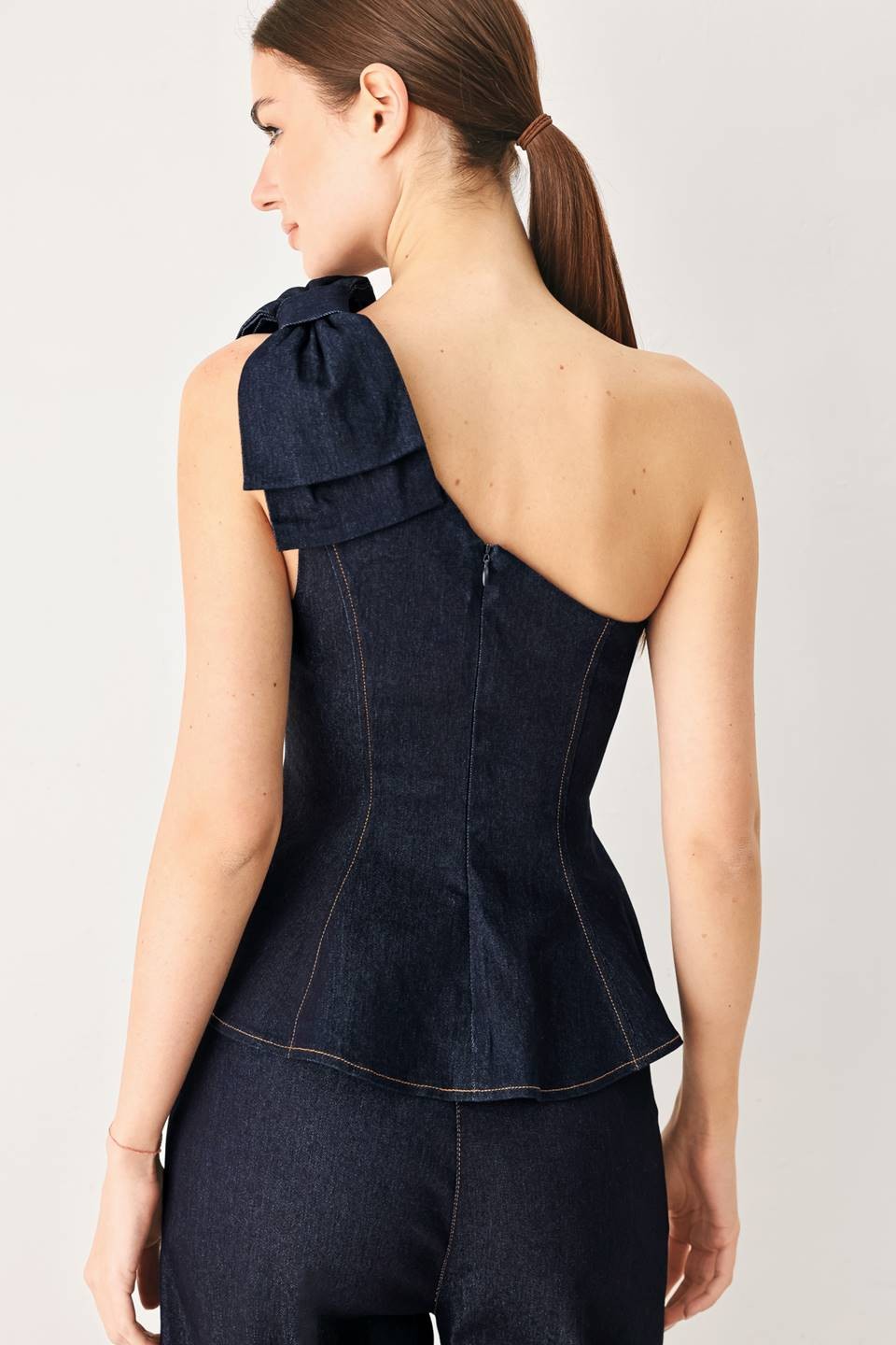 A denim top featuring one shoulder neckline with bow, peplum and back zipper