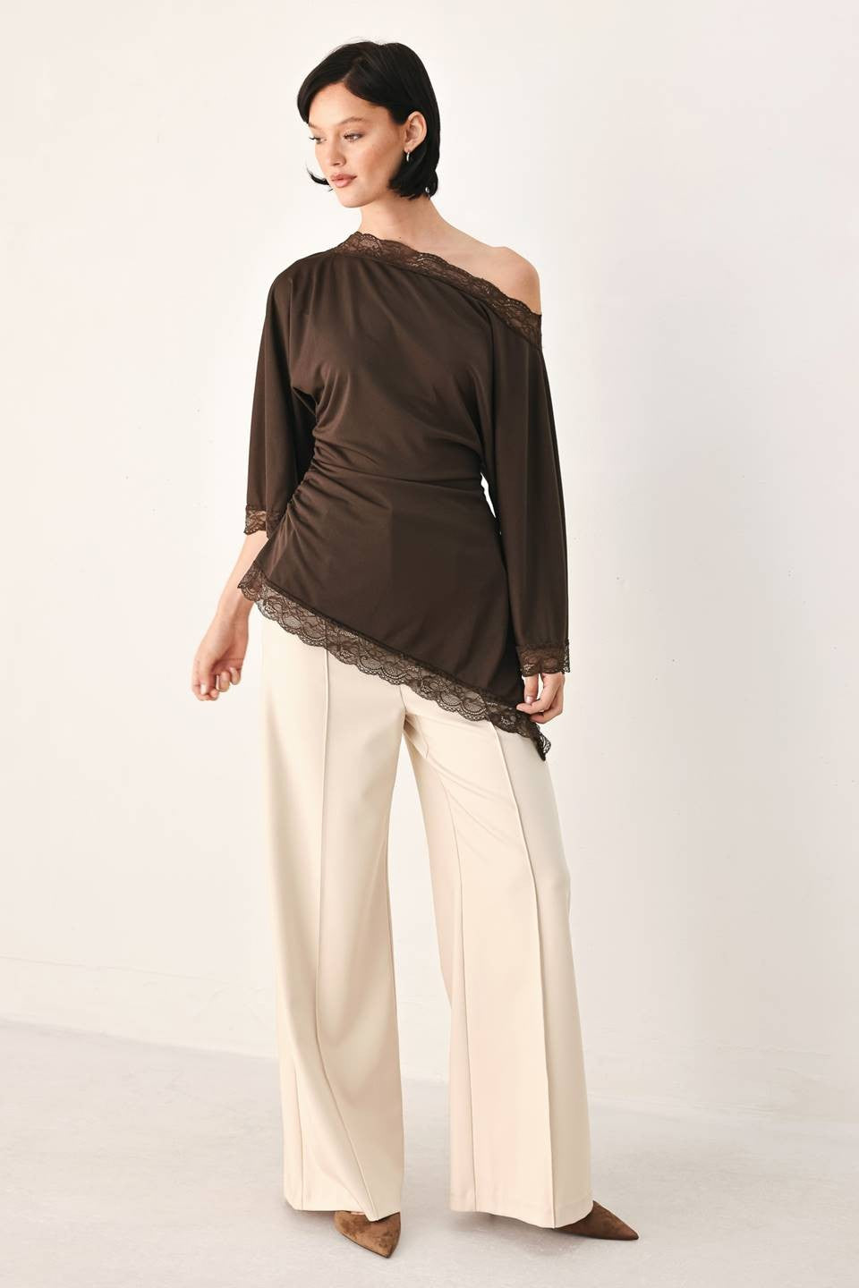 A solid knit top with boat neckline, bell sleeve, asymmetrical hem and lace edge