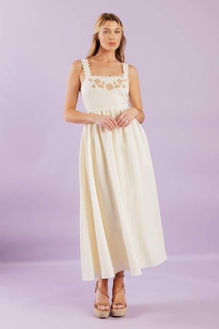 A solid woven midi dress featuring ric rac trimmed straight neckline and straps, embroidered bodice and smocked back bodice