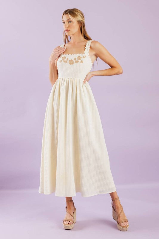 A solid woven midi dress featuring ric rac trimmed straight neckline and straps, embroidered bodice and smocked back bodice