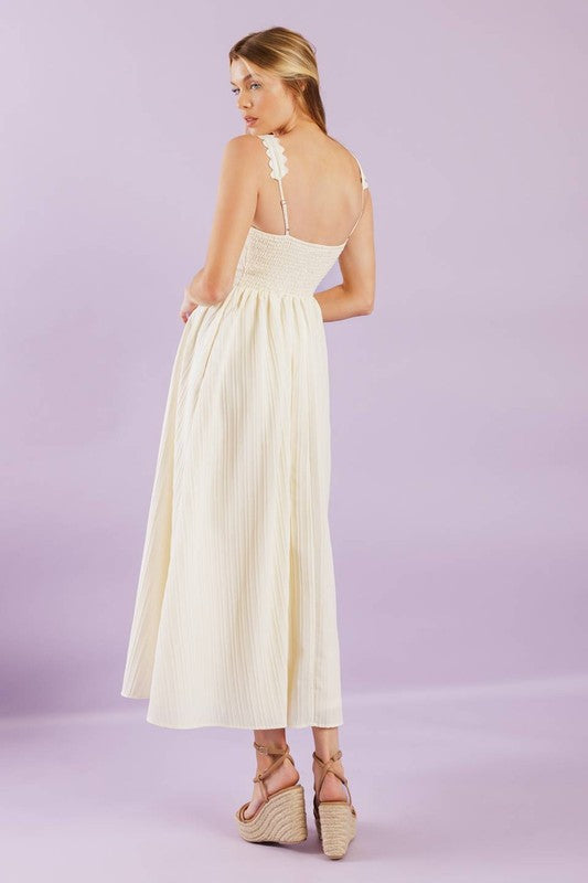 A solid woven midi dress featuring ric rac trimmed straight neckline and straps, embroidered bodice and smocked back bodice