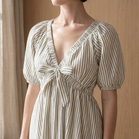 Detailed close-up of Stripe Woven Mini Dress highlighting V neckline, balloon sleeves, woven pattern, and front tie in boutique setting.