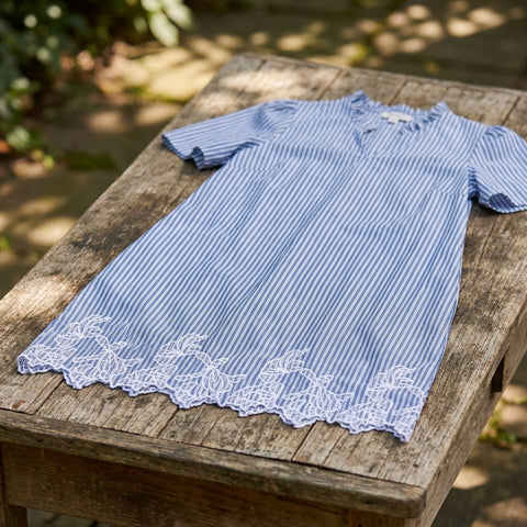 Medium shot of mini dress on a rustic wooden table highlighting embroidery and fabric details with ambient daylight.