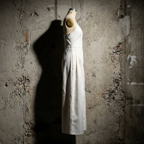 Side profile of the jumpsuit hanging against an industrial cement wall, high-contrast lighting emphasizing textured woven pattern.