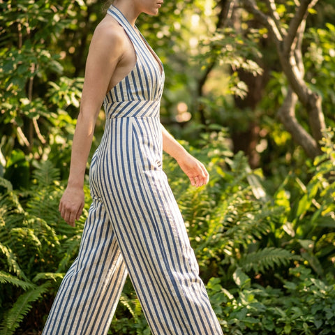 Model in Stripe Jumpsuit in outdoor scene, capturing side profile with lush greenery, sunlight, and focus on fabric details.