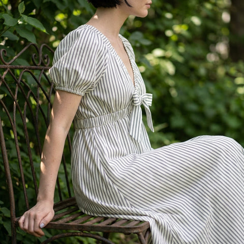 Side profile of Stripe Woven Mini Dress on seated model in greenery, showcasing V neckline, balloon sleeve, and textured fabric.